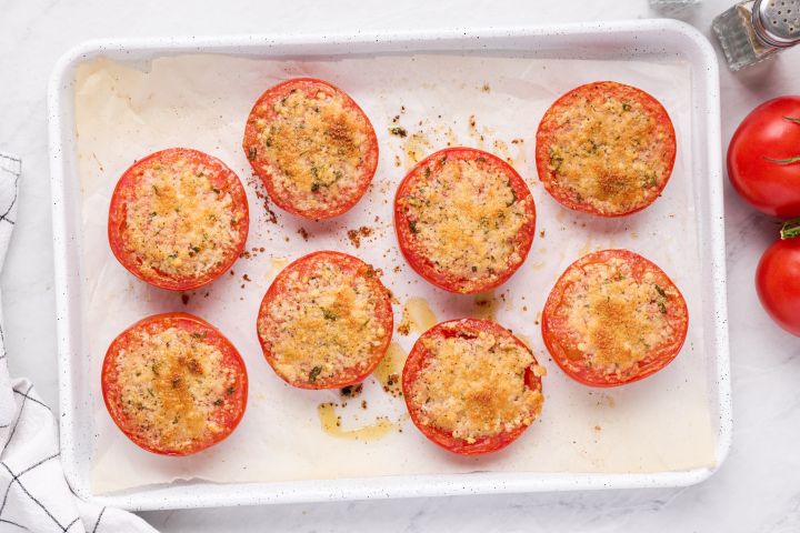 Baked parmesan tomatoes with lightly browned Parmesan cheese and herbs on a white baking sheet.