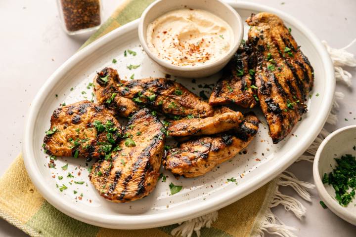 Platter of balsamic grilled chicken breasts and tenders topped with chopped parsley and served with a creamy dipping sauce.