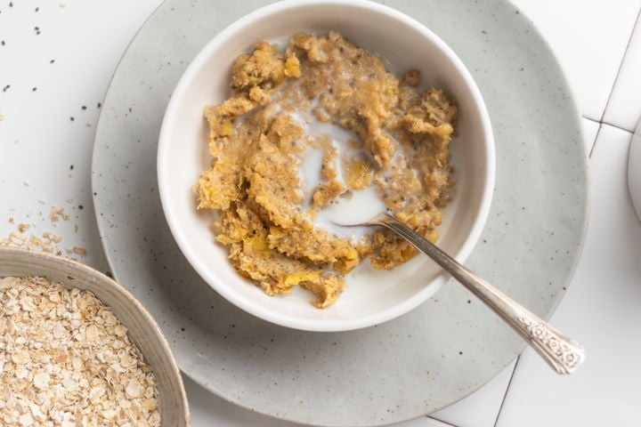 Banana protein oatmeal made with rolled oats, mashed banana, chia seeds, and almond milk served in a bowl with a spoon.