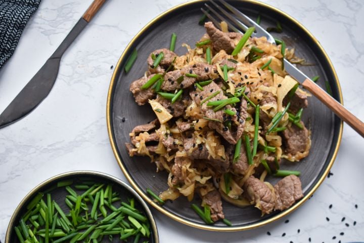 Beef and cabbage stir fry with garlic, green onions, and sesame seeds on a plate with chopsticks.