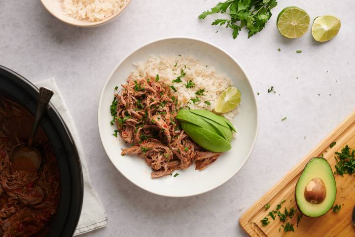 Beef machaca served with white rice in a bowl with cilantro and avocado on top.