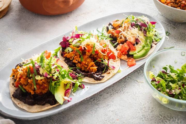 Beef tostadas with ground beef, refried beans, avocado, salsa, lettuce, tomato, and cheese on a plate.