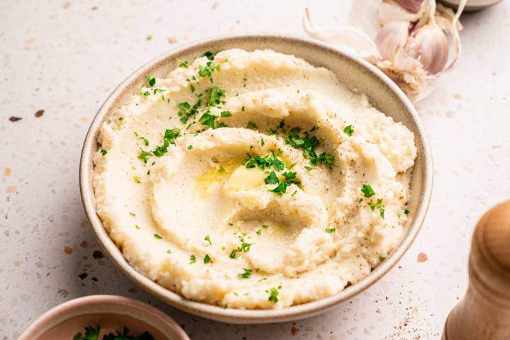 A bowl of creamy mashed cauliflower topped with melted butter and chopped parsley.