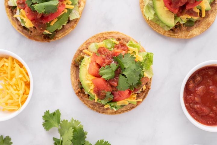 Tostadas with beans, cooked meat, shredded lettuce, tomatoes, avocado, and salsa.
