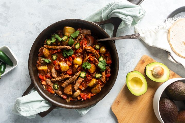 Bistec ranchero with pieces of steak cooked in a tomato and pepper sauce in a skillet.