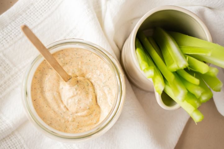 Blackened ranch dressing with yogurt and buttermilk in a glass jar with celery sticks.