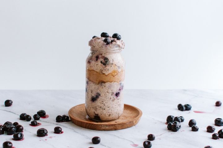 Blueberry overnight oatmeal with almond butter in a mason jar with blueberries on the side.