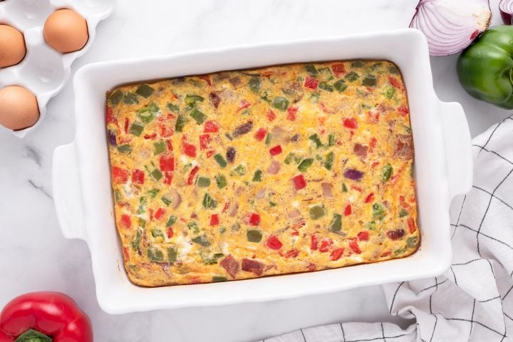 Breakfast egg casserole with turkey bacon, cheddar cheese, peppers, and onions in a baking dish.