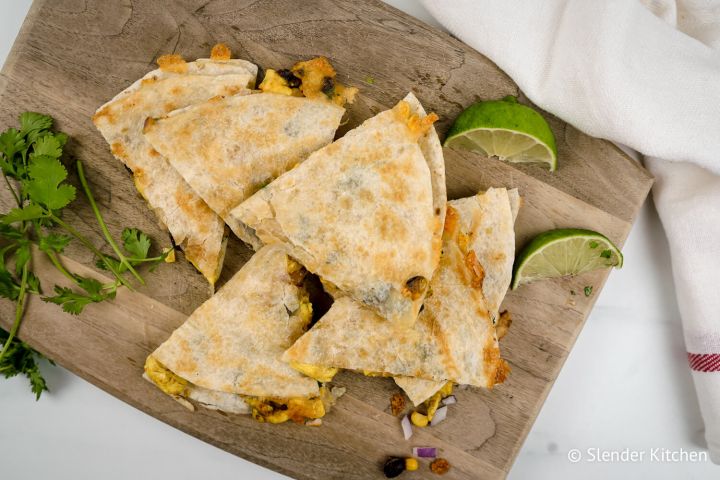 Breakfast quesadillas with eggs, corn, black beans, and cilantro on a cutting board.