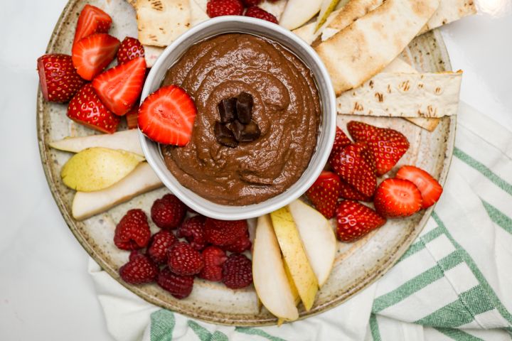 Brownie batter hummus in a bowl with cut fruit and crackers.