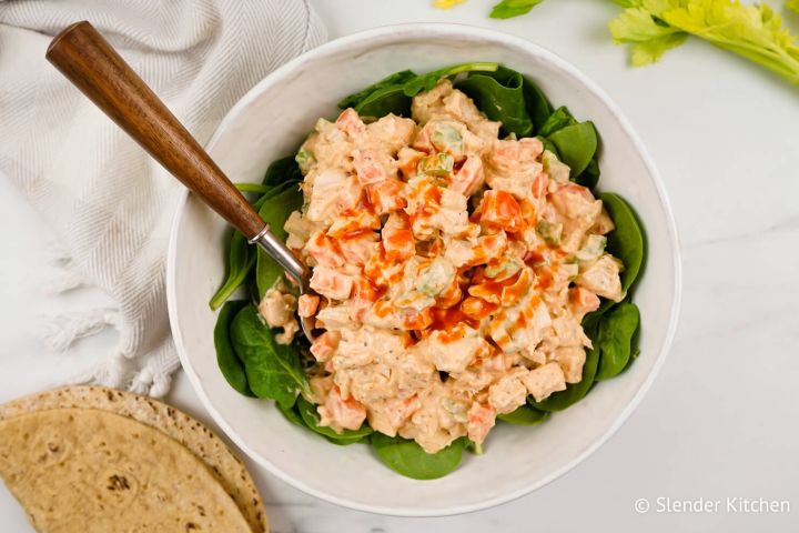 Buffalo chicken salad with fresh spinach, a whole wheat wrap, and a spoon in a bowl.