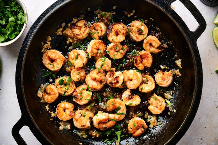 Camarones al mojo de ajo in a skillet with juicy shrimp, garlic, onion, butter, lime juice, and fresh parsley.