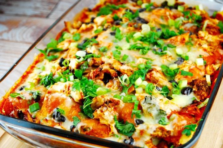 Chicken enchilada casserole with green onions and olives in a baking dish.