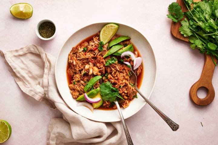 Chicken machaca served in a bowl with shredded chicken in spicy tomato sauce with limes and red onion.