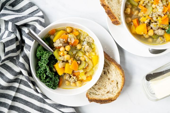 Chickpea stew with turkey sausage and butternut squash in a white bowl with bread on the side.