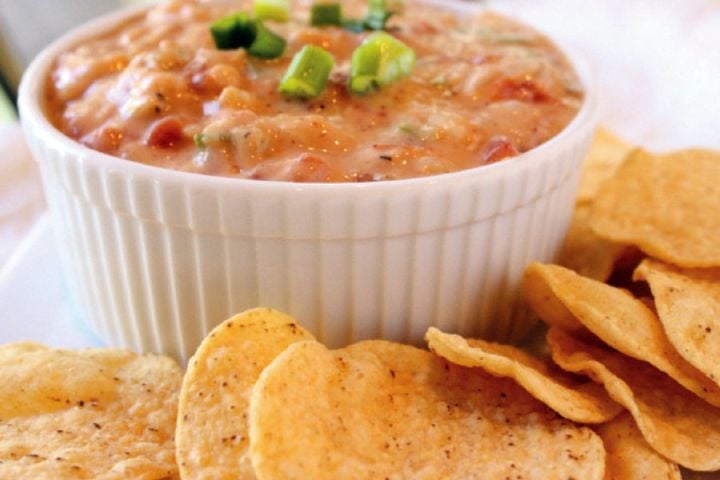 Chili con queso in a bowl with melted cheese, chilies, green onions, and tortilla chips.