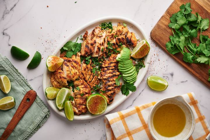 Chili lime chicken breast sliced and served on a wooden cutting board with lime and cilantro.
