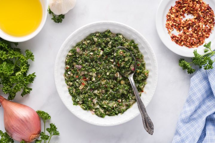 Chimichurri sauce with parsley, garlic, olive oil, red wine vinegar, and shallots mixed together in a small bowl.