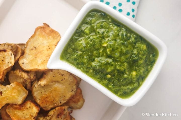 Cilantro pesto in a small white container with cilantro leaves, olive oil, lemon juice, and Parmesan cheese.