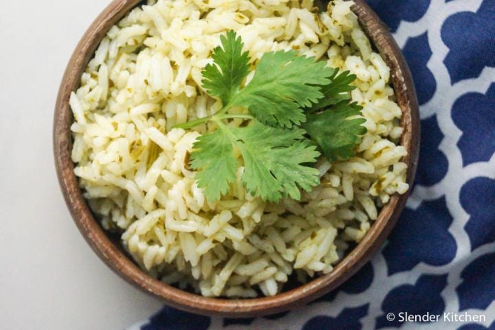 Garlic cilantro brown rice in a bowl with fresh cilantro leaves and lime wedges. 