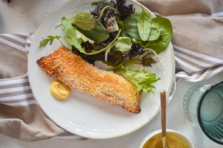 Coconut crusted salmon coated with crispy shredded coconut and spices on a plate with a mixed green salad.