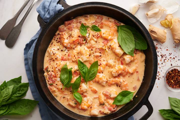 Creamy coconut shrimp with tomatoes, coconut milk, basil, and red pepper flakes in a black skillet.