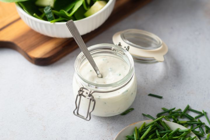 Creamy gorgonzola dressing with chunks of gorgonzola cheese, Greek yogurt, chives, and buttermilk in a small glass jar.
