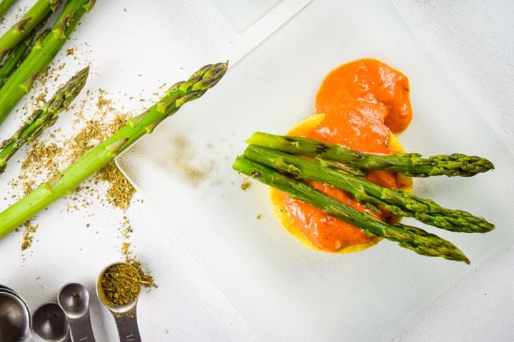 Crispy polenta with asparagus in a creamy tomato sauce on a clear plate with herbs.