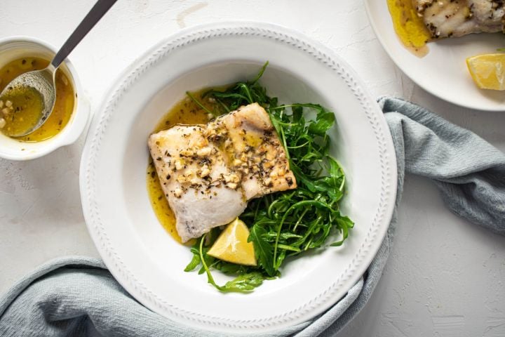 Easy baked cod with a lemon, garlic, and butter sauce on a white plate with mixed greens.