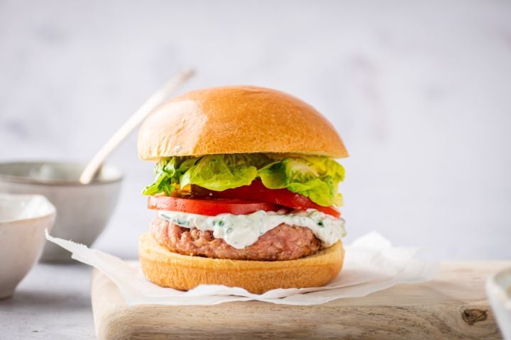 Ground chicken burger with ranch dressing, tomatoes, and lettuce on a burger bun.