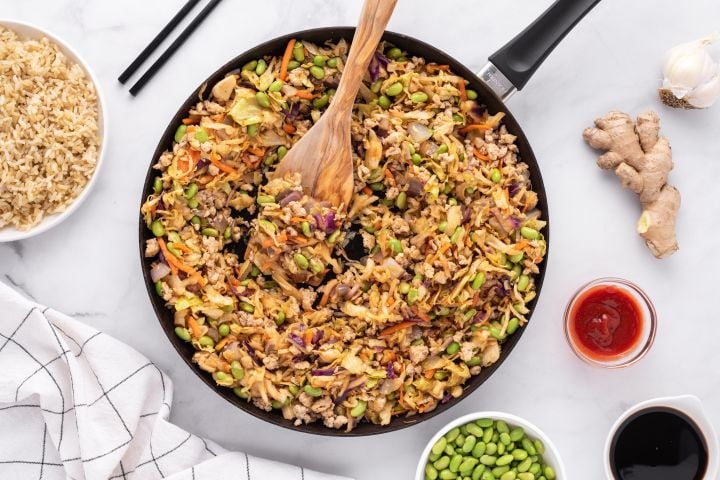 Egg roll in a bowl with ground chicken, shredded cabbage, and an Asian sauce.