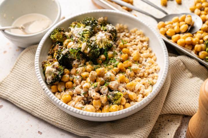 A bowl of roasted broccoli, chickpeas, and grains topped with a creamy sauce. 