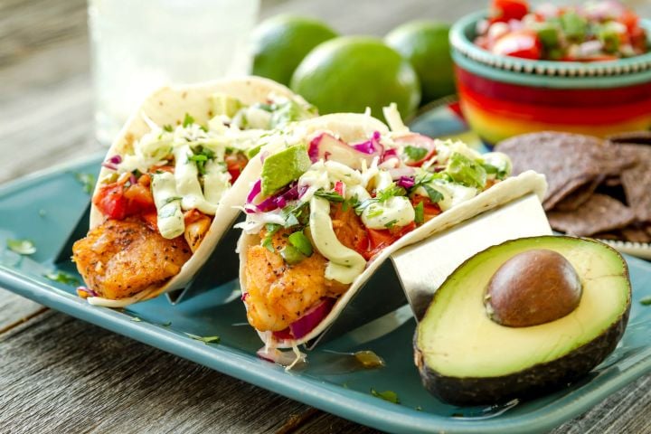  Easy fish tacos with avocado cream on two corn tortillas with a fork and green napkin.