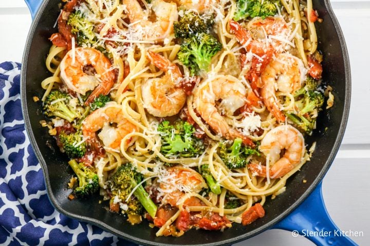 Garlic lemon and shrimp and broccoli pasta in a pan with fresh lemon slices and Parmesan cheese.