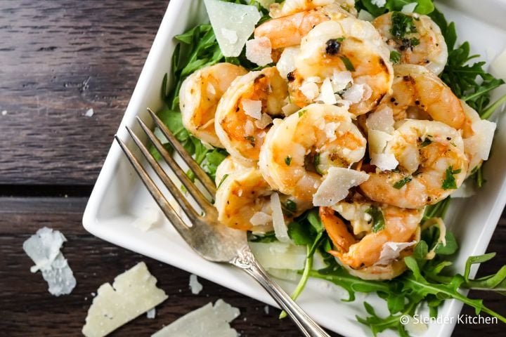 Garlic Parmesan shrimp on a plate with pieces of Parmesan cheese and greens.