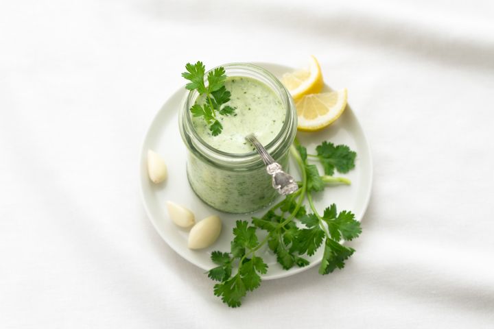 Green goddess dressing in a glass jar with fresh cilantro, garlic, and lemon on the side.