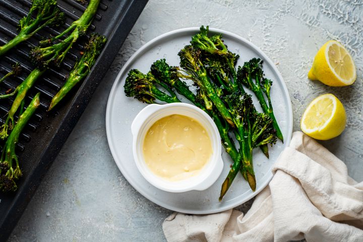 Garlic grilled broccolini served on a plate with fresh lemon and garlic aioli 