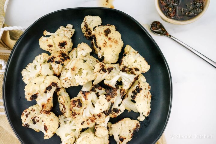 Grilled cauliflower with browned edges on a plate with fresh parsley.