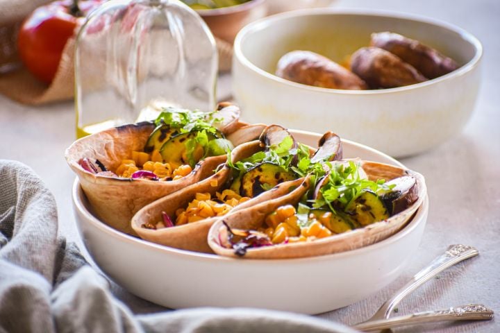 Veggie tacos tacos with mushrooms, corn, and zucchini in a wheat taco shell in a bowl. 