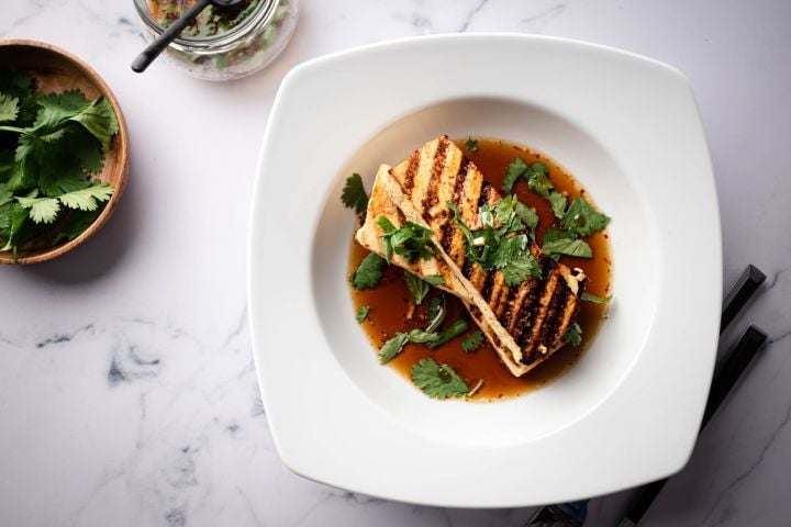Grilled tofu in a marinade made with soy sauce served in a bowl with cilantro.