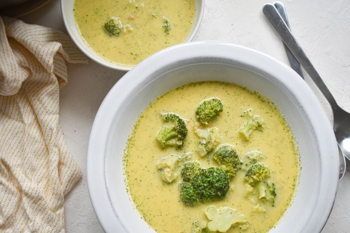 Healthy Broccoli Cheese Soup with broccoli florets, cheddar cheese, and a creamy broth in two bowls.