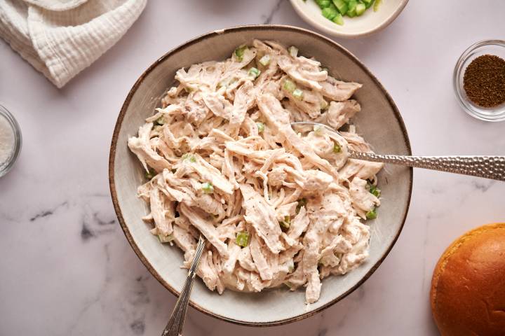 Healthy chicken salad with shredded chicken, celery, greek yogurt, mayonnaise, and spices in a bowl.