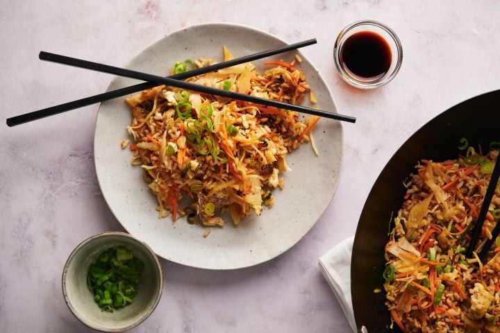 Healthy fried rice with cabbage, carrots, and vegetables served on a plate with chopsticks and in a wok.