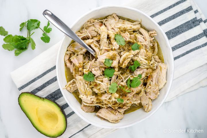 Instant Pot Salsa chicken shredded in a bowl with green salsa and cilantro.