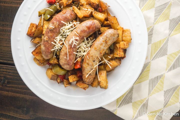 Roasted sausages with potatoes, peppers, and onions on a plate with Parmesan cheese.