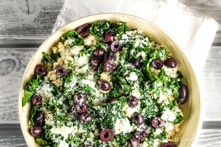 Kale caesar quinoa bowl with shredded kale, cooked quinoa, creamy Caesar dressing, and black olives in a wooden bowl.