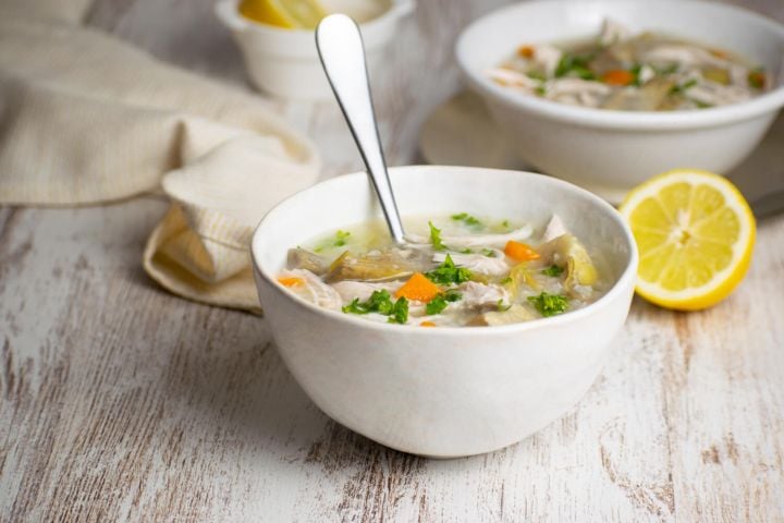 Slow cooker lemon artichoke chicken soup with rice in a bowl with carrots and lemon.