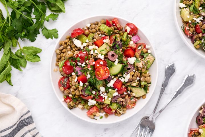 Easy lentil salad with Mediterranean flavors including olives, feta cheese, tomatoes, cucumbers, and fresh herbs in a bowl.