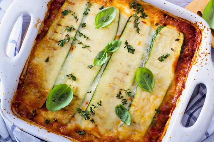 Low carb zucchini lasagna in a baking dish with zucchini slices, marinara sauce, and melted cheese. 