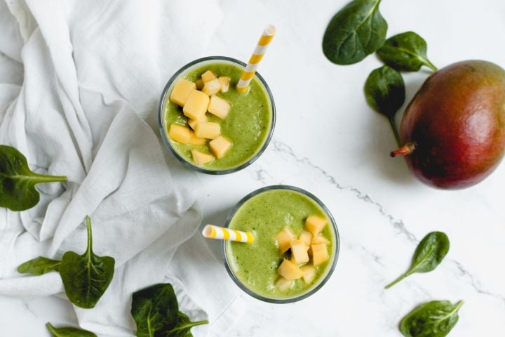 Mango spinach smoothie in two cups with fresh mango chunks on top.